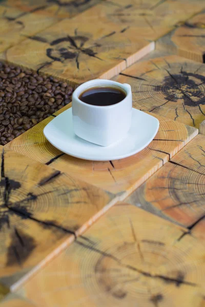 Small white cup of coffee and roasted coffee beans on wooden background from saw cut wood — Stock Photo, Image