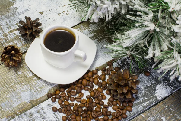 Mała biała filiżanka kawy, Palone ziarna kawy i gałąź Jodłowa w śniegu z stożkiem na drewnianym tle — Zdjęcie stockowe