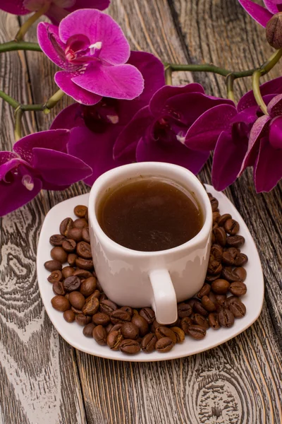 Small white cup of coffee, roasted coffee beans, orchid on wooden background — Stock Photo, Image