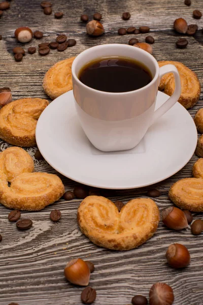 Kleine weiße Tasse Kaffee, Haselnüsse, Kakaobohnen, Kekse auf Holzgrund lizenzfreie Stockfotos