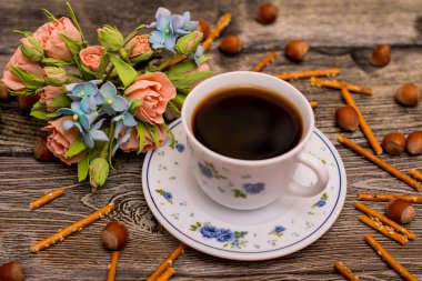 Küçük beyaz fincan kahve, fındık, kakao çekirdekleri, çerezler ve buket çiçek ahşap arka plan üzerinde