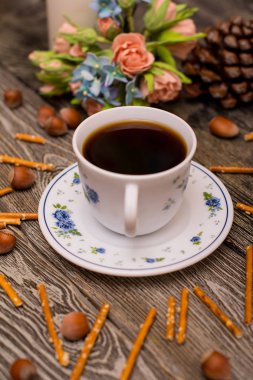 Küçük beyaz fincan kahve, fındık, kakao çekirdekleri, çerezler ve buket çiçek ahşap arka plan üzerinde