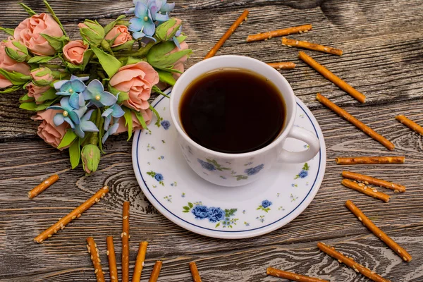 Kleine weiße Tasse Kaffee, Haselnüsse, Kakaobohnen, Kekse und Blumenstrauß auf Holzgrund Stockbild