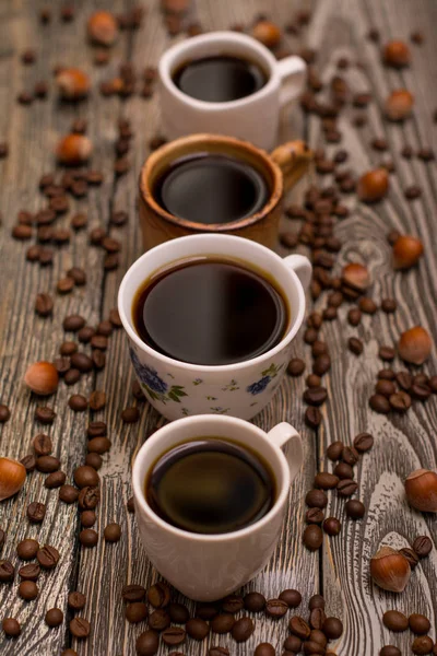 Four cups of coffee, hazelnuts and cocoa beans on wooden background — Stock Photo, Image
