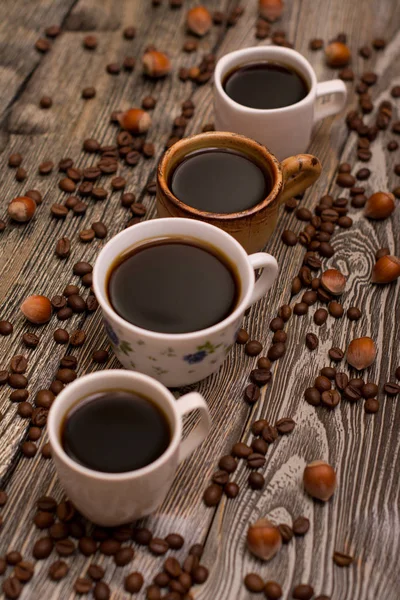 Quattro tazze di caffè, nocciole e fave di cacao su fondo di legno — Foto Stock