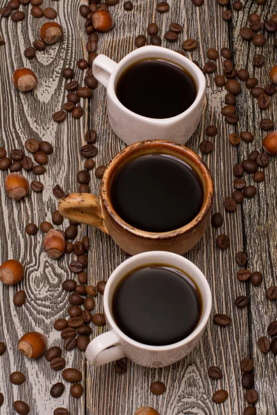 Tre tazze di caffè, nocciole e fave di cacao su fondo di legno — Foto Stock