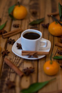 Küçük beyaz fincan kahve, tarçın, yıldız anason ve ahşap zemin üzerine mandalina