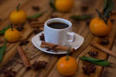 Küçük beyaz fincan kahve, tarçın, yıldız anason ve ahşap zemin üzerine mandalina