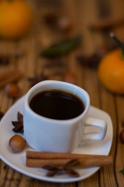 Küçük beyaz fincan kahve, tarçın, yıldız anason, fındık ve ahşap zemin üzerine mandalina