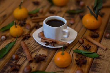 Küçük beyaz fincan kahve, tarçın, yıldız anason, fındık ve ahşap zemin üzerine mandalina