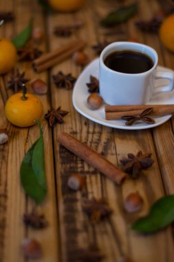 Küçük beyaz fincan kahve, tarçın, yıldız anason, fındık ve ahşap zemin üzerine mandalina