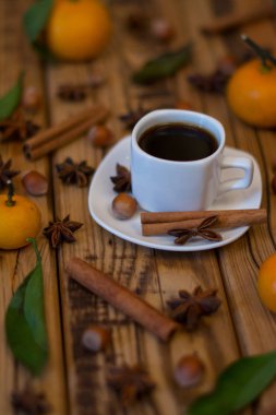 Küçük beyaz fincan kahve, tarçın, yıldız anason, fındık ve ahşap zemin üzerine mandalina