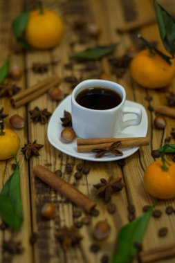 Küçük beyaz fincan kahve, tarçın, kakao çekirdekleri, yıldız anason, fındık ve ahşap zemin üzerine mandalina