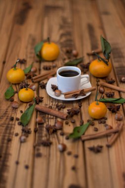 Küçük beyaz fincan kahve, tarçın, kakao çekirdekleri, yıldız anason, fındık ve ahşap zemin üzerine mandalina