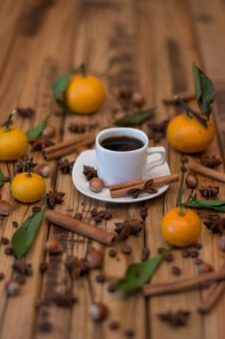 Küçük beyaz fincan kahve, tarçın, kakao çekirdekleri, yıldız anason, fındık ve ahşap zemin üzerine mandalina