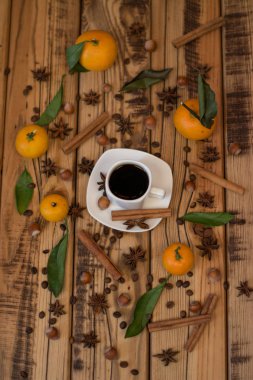 Küçük beyaz fincan kahve, tarçın, kakao çekirdekleri, yıldız anason, fındık ve ahşap zemin üzerine mandalina