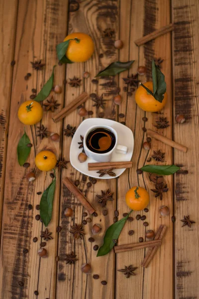 Malý bílý šálek kávy, skořice hole, kakaové boby, badyánu, lískových ořechů a mandarinky na dřevěné pozadí — Stock fotografie