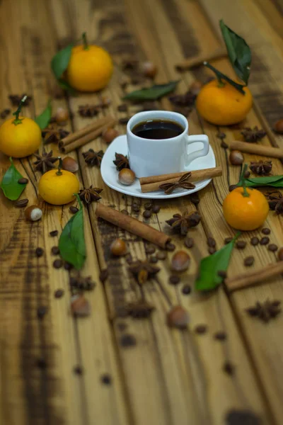 Malý bílý šálek kávy, skořice hole, kakaové boby, badyánu, lískových ořechů a mandarinky na dřevěné pozadí — Stock fotografie