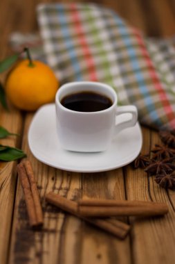 Küçük beyaz fincan kahve, tarçın, yıldız anason ve mandarin ahşap arka plan üzerinde