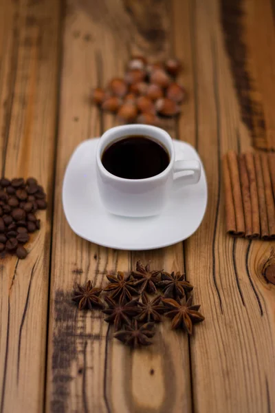 Malý bílý šálek kávy, skořice hole, kakaových bobů, badyánu, lískové ořechy na dřevěné pozadí — Stock fotografie