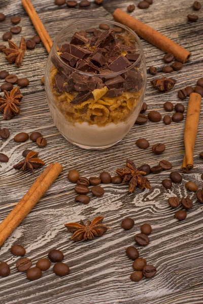 Postres de yogur con chocolate y galletas, palitos de canela, granos de cacao, anís estrellado sobre fondo de madera — Foto de Stock