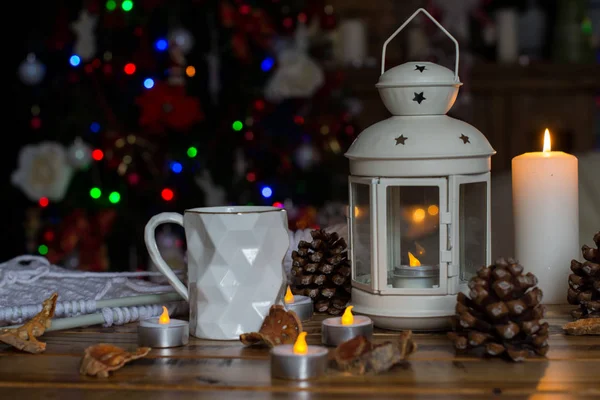 Decorações de Natal com lâmpada com vela, caneca branca, cítricos secos, cone na mesa de madeira contra fundo luzes — Fotografia de Stock