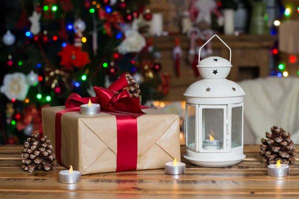 Weihnachtsdekoration. Geschenkkarton, Lampe mit Kerze, Kegel auf Holztisch vor Lichterhintergrund Stockfoto