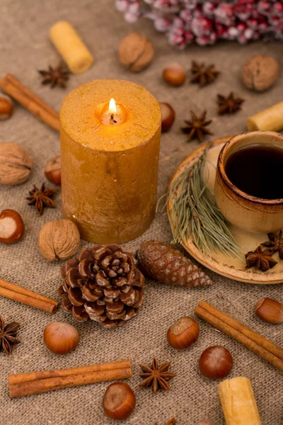 Cup of coffee, cookies, walnuts, hazelnuts, cinnamon sticks, star anise, cone, candle, fir branch on sackcloth fabric — Stock Photo, Image