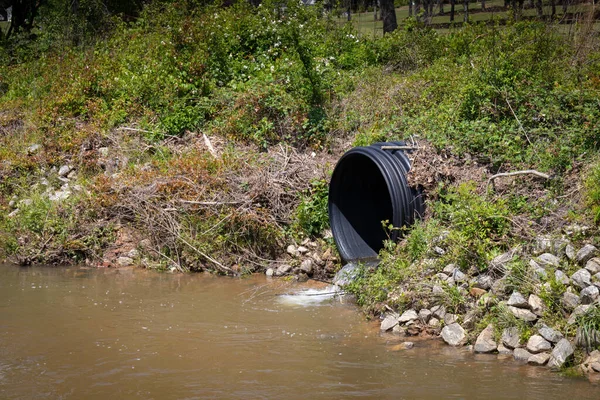 Siyah plastik kanalizasyon borusu bir dereye su salıyor, çevresel güvenlik sorunu, yatay görünüm