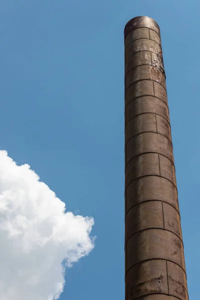 Single smoke stack stretching high into blue sky with cloud, copy space, vertical aspect