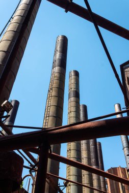 Tütsü bacaları, borular ve kirişler mavi gökyüzüne karşı, eski endüstriyel kompleks, dikey görünüm