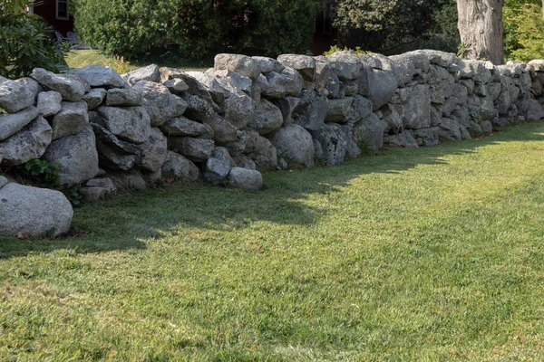 Yeşil çimenler ve olgun çalılar yığılmış bir taş duvarla ayrılmış, yatay görünüm