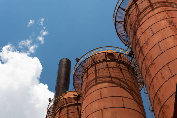 Sloss Furnaces National Historic Landmark, Birmingham Alabama USA, orange rusty furnaces seen from below, silhouetted against a blue sky with clouds, horizontal aspect