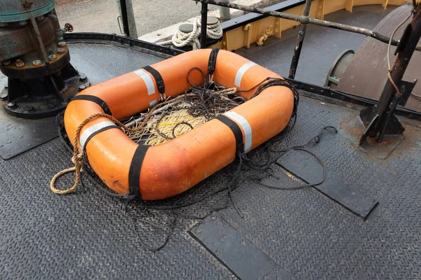 Small orange rescue life raft with mesh bottom on the deck of a boat, metal diamondplate painted black, copy space, horizontal aspect