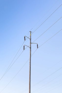 Mavi gökyüzüne karşı gerilim yalıtıcılarıyla asılmış tek elektrik direği, kopyalama alanı, dikey görünüm