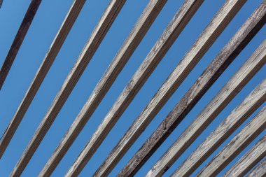 Mavi gökyüzüne karşı eskimiş ahşap kirişlerin belirsiz görüntüsü, soyut arka plan deseni, yatay görünüm