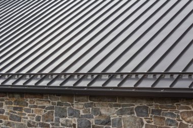Standing seam modern metal roof over vintage stone wall, horizontal aspect clipart