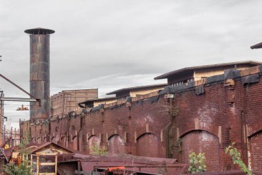 Depo bölgesinin dış görünüşü, eski tuğla mimarisi, baca, paslanmış metal yapılar, yatay görünüm.