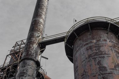 Gri gökyüzüne karşı baca ve yürüme yolları, endüstriyel üretim mimarisi, yatay görünüm