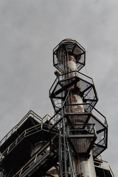 Ladders and expanded metal walkways around a smokestack, urban industrial steel mill, vertical aspect