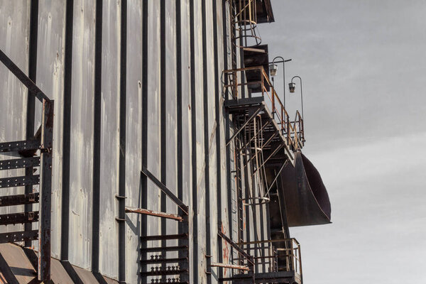 Wall of steel panels, walkways and ladders, gray skies, horizontal aspect