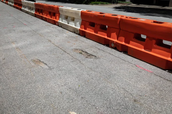 Line of orange and white hard plastic traffic barricades dividing a city street, crumbling asphalt roadway, creative copy space, horizontal aspect