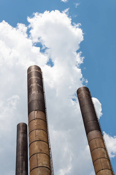 Three extremely tall smokestacks seen from below against a blue sky with clouds, hopeful industrial image with creative copy space, vertical aspect
