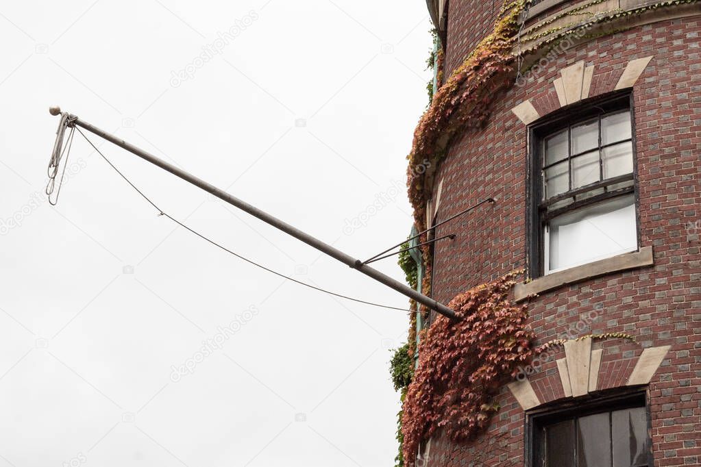 Flag pole extending from the face of a brick brownstone building with ivy on face, horizontal aspect