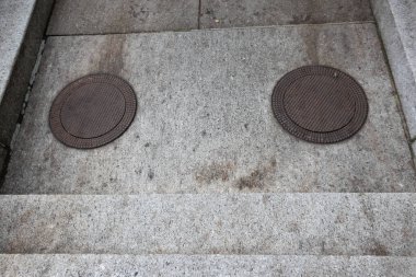 Beton merdivenlerin çıkışında bir çift demir metal rögar kapağı var.