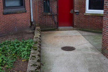 Beton geçitli, yatay görünümlü eski tuğla apartmanın kırmızı kapısı.