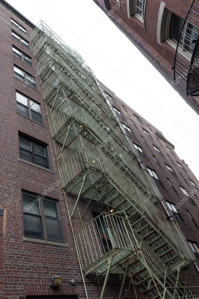 Extreme upward view of caged fire escape in an alley between two urban housing units, vertical aspect