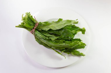 Beyaz bir tabakta kırmızı ve kenevir sicimi ile bağlanmış bir grup yeşil kabuklu yaprak, beyaz, yatay görünümde izole.