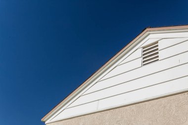 Yan ve çatı kenarı genel ev görüntüsü, tavan arası havalandırması derin mavi gökyüzüne ayarlanmış sıva ve vinil, kopyalama alanı, yatay görünüm