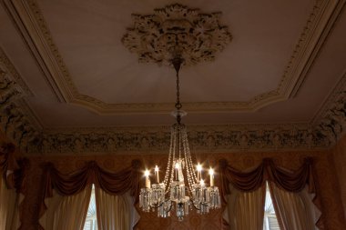 Şatafatlı perdeleri, alçı kalıpları, yumuşak renkleri, yatay görünümü olan güzel bir odada kristal bir avize.